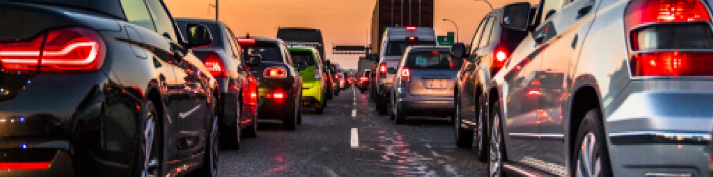Car accidents happen often in the US. Know how many car crashes a year and car accident statistics before getting on the road. Image is of cars driving on highway at dusk. Photo is taken of behind cars; head lights are all on. Sky is orange and road is asphalt. There are many cars on the road.