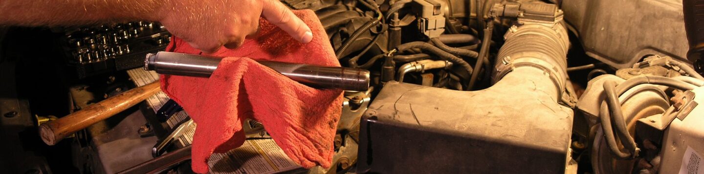 Understanding vehicle recalls and what you need to know to keep your car safe. Photo is of a car engine, the hood is up and someone is holding a red towel and a mechanics tool above the engine, looking like they are working on it.