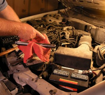 Understanding vehicle recalls and what you need to know to keep your car safe. Photo is of a car engine, the hood is up and someone is holding a red towel and a mechanics tool above the engine, looking like they are working on it.