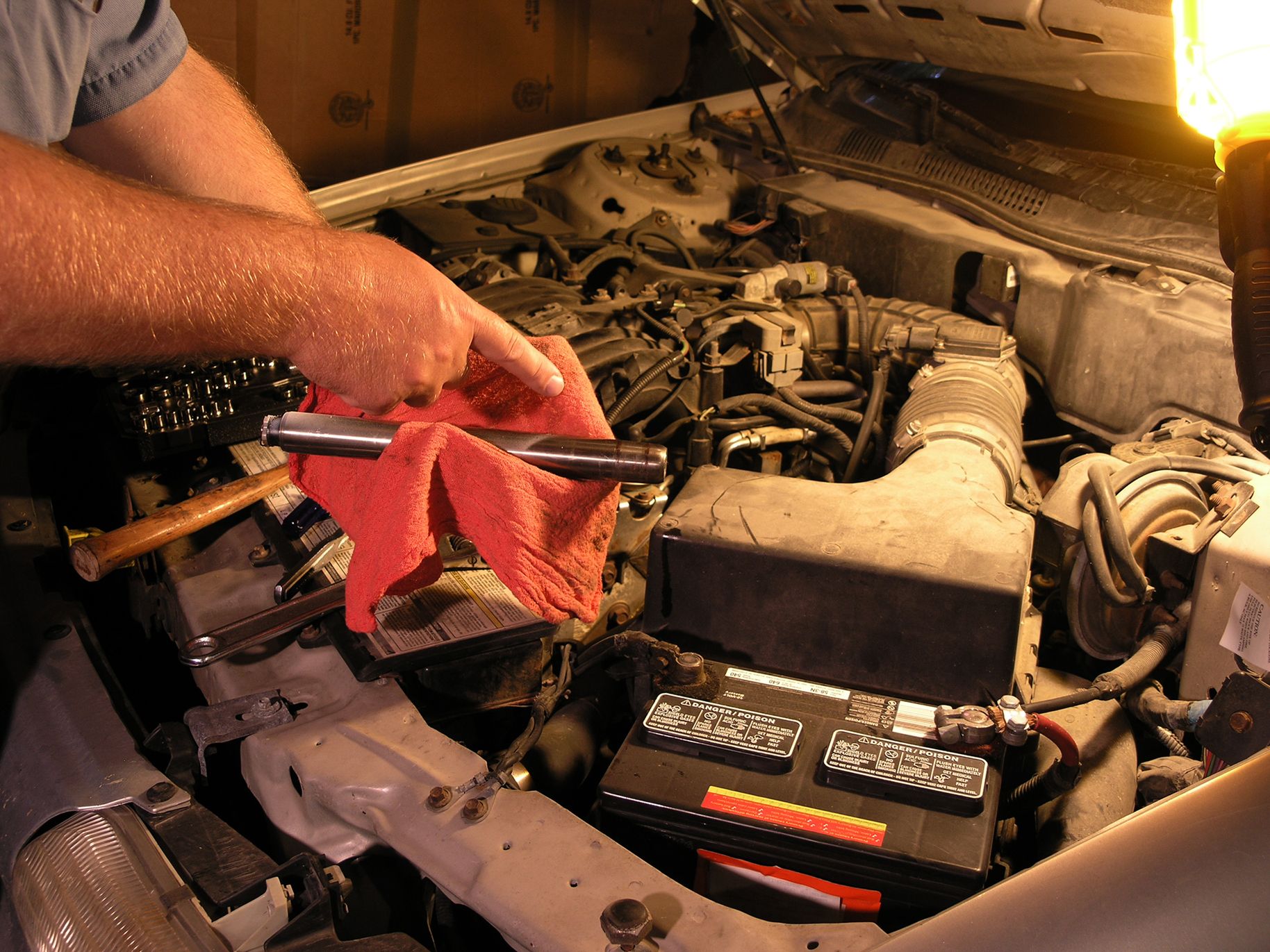 Understanding vehicle recalls and what you need to know to keep your car safe. Photo is of a car engine, the hood is up and someone is holding a red towel and a mechanics tool above the engine, looking like they are working on it.