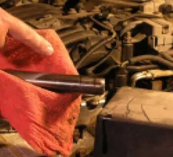 Understanding vehicle recalls and what you need to know to keep your car safe. Photo is of a car engine, the hood is up and someone is holding a red towel and a mechanics tool above the engine, looking like they are working on it.