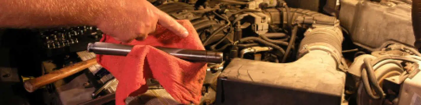 Understanding vehicle recalls and what you need to know to keep your car safe. Photo is of a car engine, the hood is up and someone is holding a red towel and a mechanics tool above the engine, looking like they are working on it.