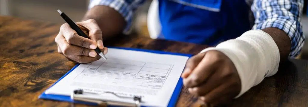 A worker with a cast on their arm filling out workers’ comp papers.