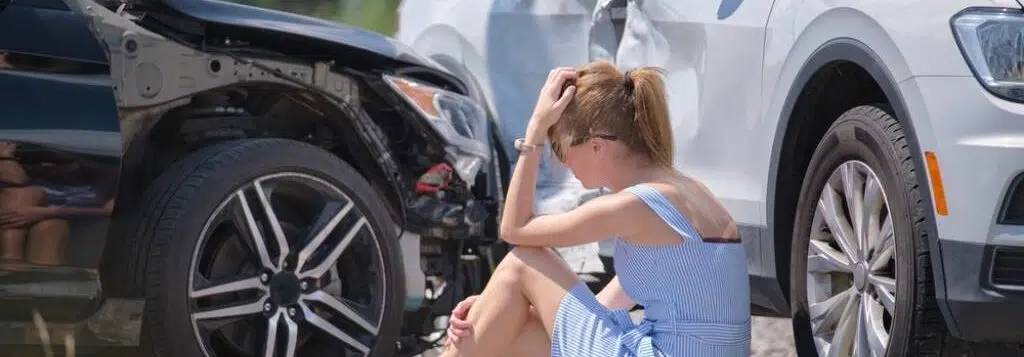 A woman sitting on the ground holding her head and leg after a car accident